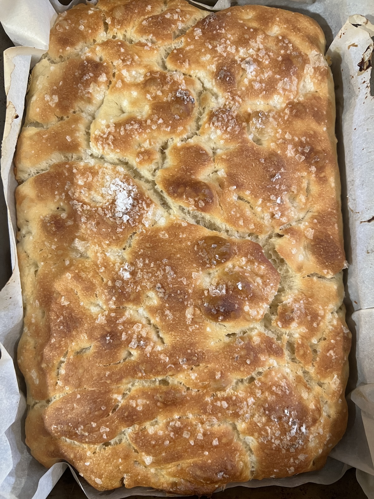 over head view of golden brown focaccia topped with flaky sea salt in a 9x13 baking pan